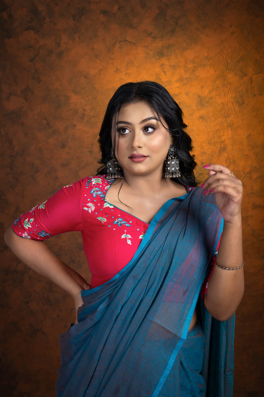 Model wearing a pink glazed cotton blouse with multicolor floral embroidery and square V neckline, styled with a teal saree, posing with one hand on hip and other near face