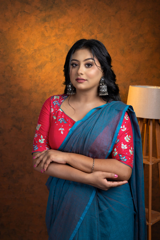 Model wearing a pink embroidered cotton blouse with floral threadwork and square V neckline, paired with a teal saree, posing with arms crossed