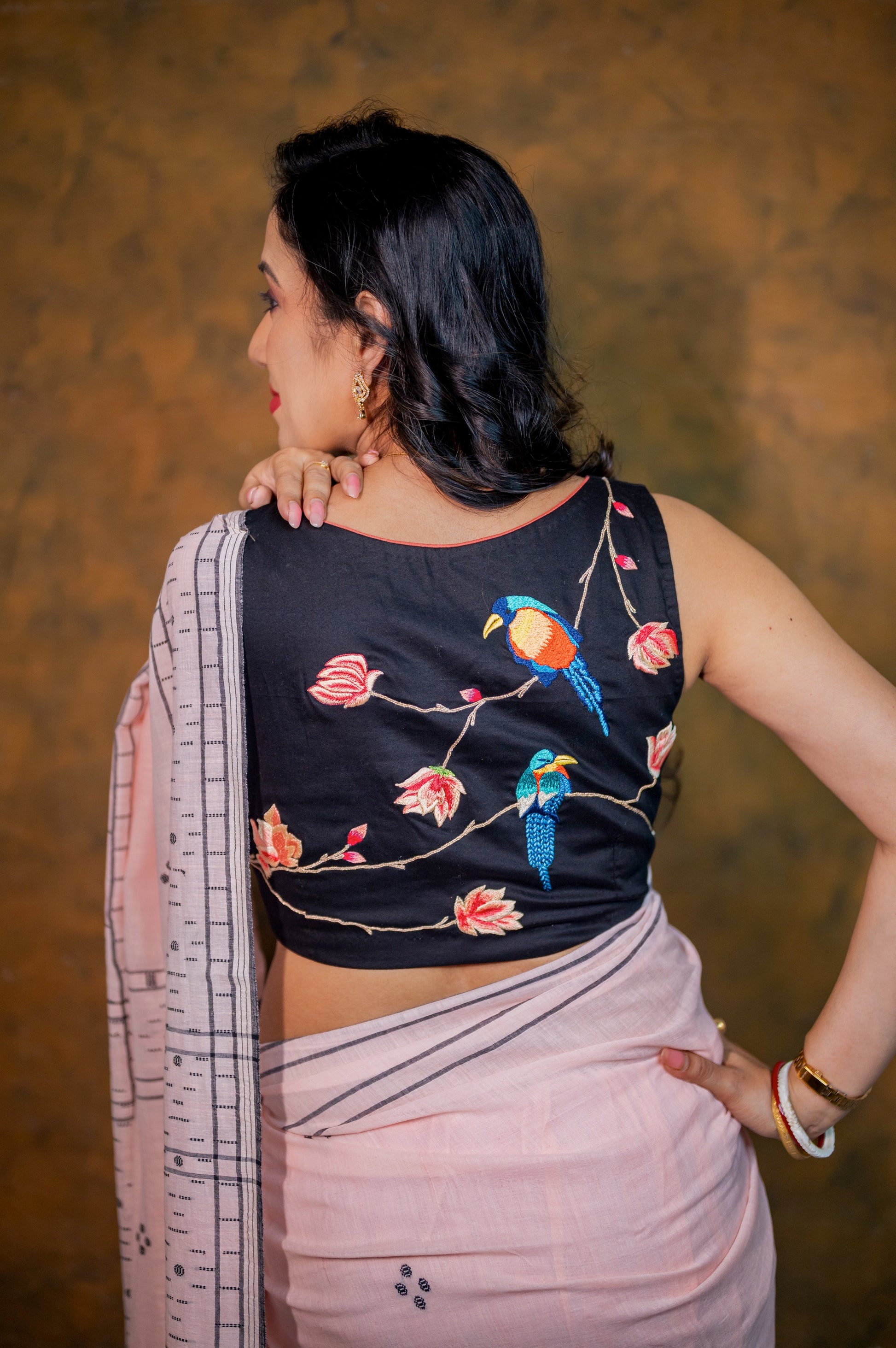 Close-up of back embroidery on a black cotton-linen blouse featuring colorful birds and blooming flowers.