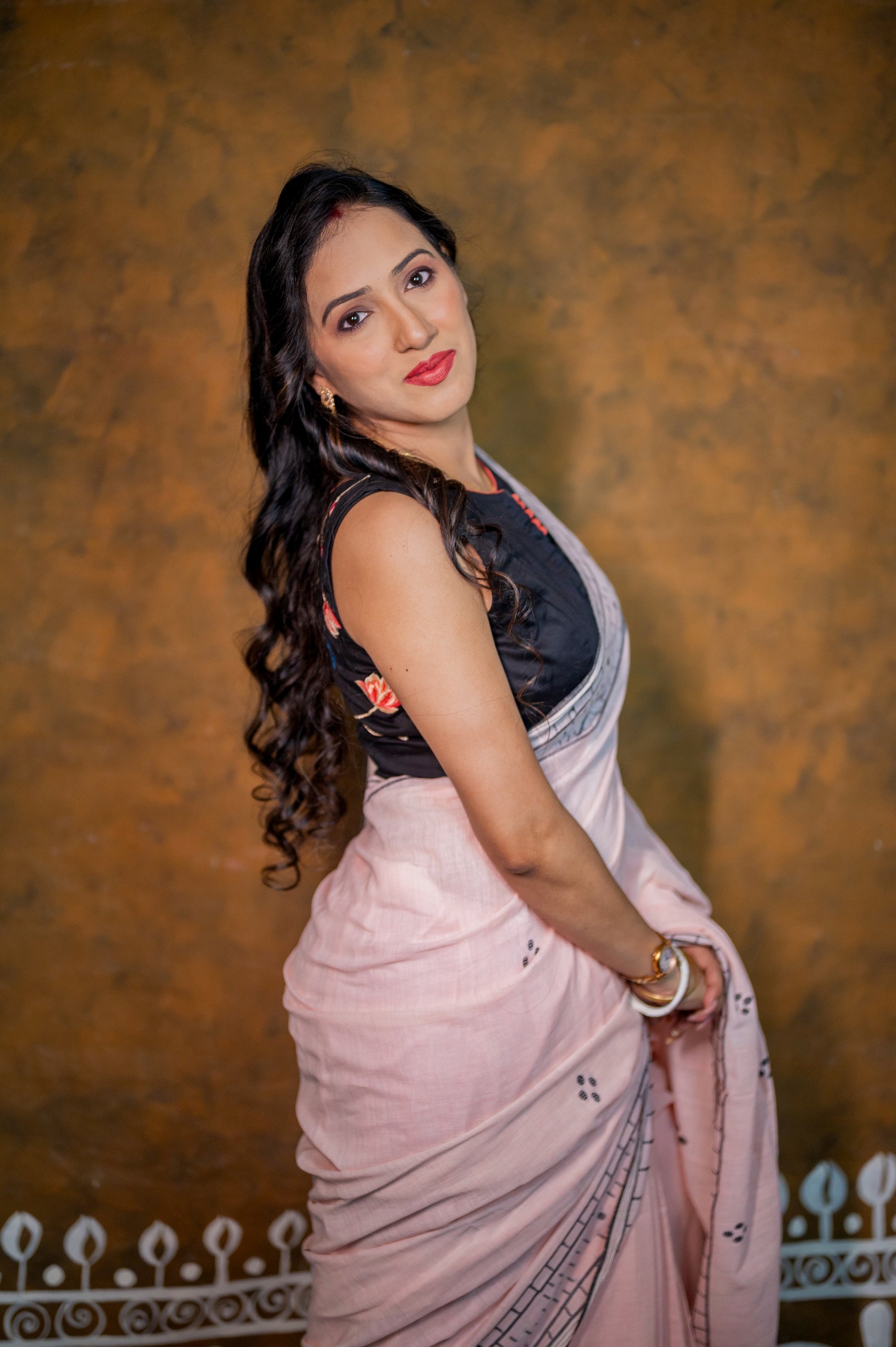 Side view of a woman wearing a black embroidered blouse and pale pink saree, highlighting the sleeveless cut.