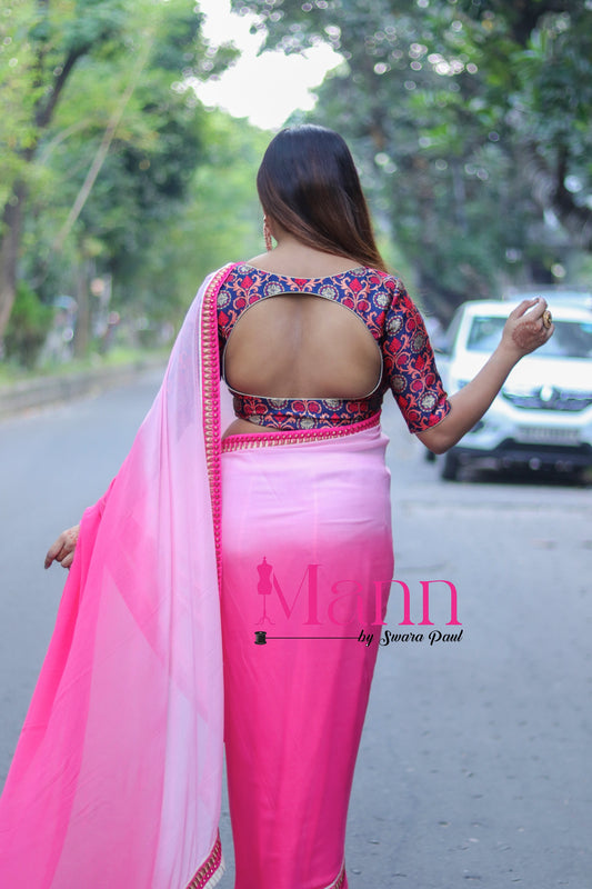 Back view of Banarasi blouse with rich multicolor motifs and curved designer cut-out, styled with a pink ombré saree, model walking down a tree-lined street