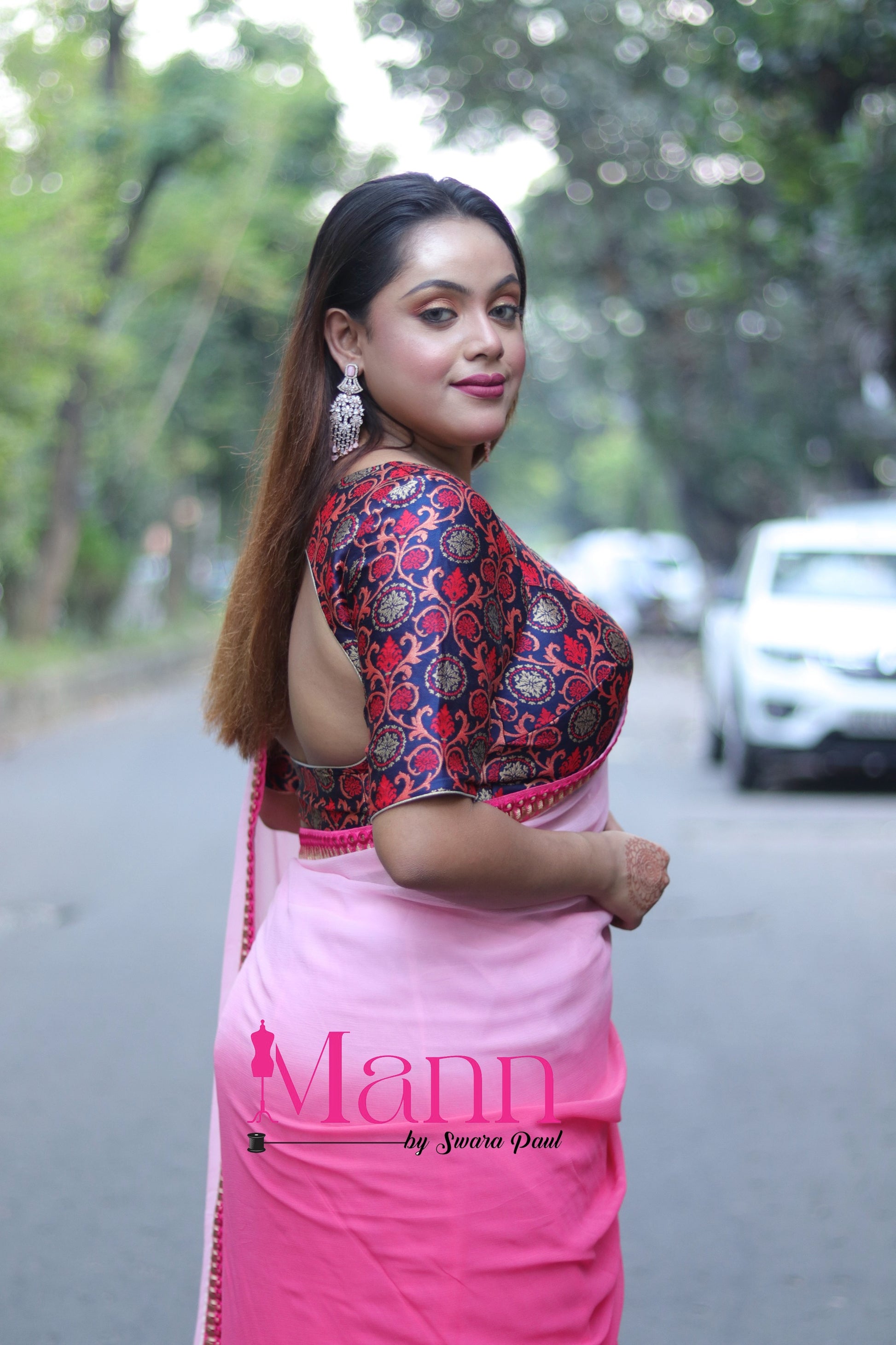 Side view of Banarasi blouse with multicolor woven accents and bold square V neckline, paired with a pink saree, model posing confidently on a city street