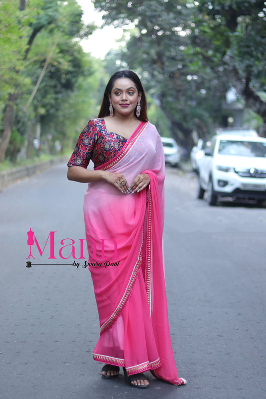 Front view of Banarasi blouse featuring bold square neckline and colorful brocade work, paired with a bright pink saree and statement jewellery, model standing on an urban road