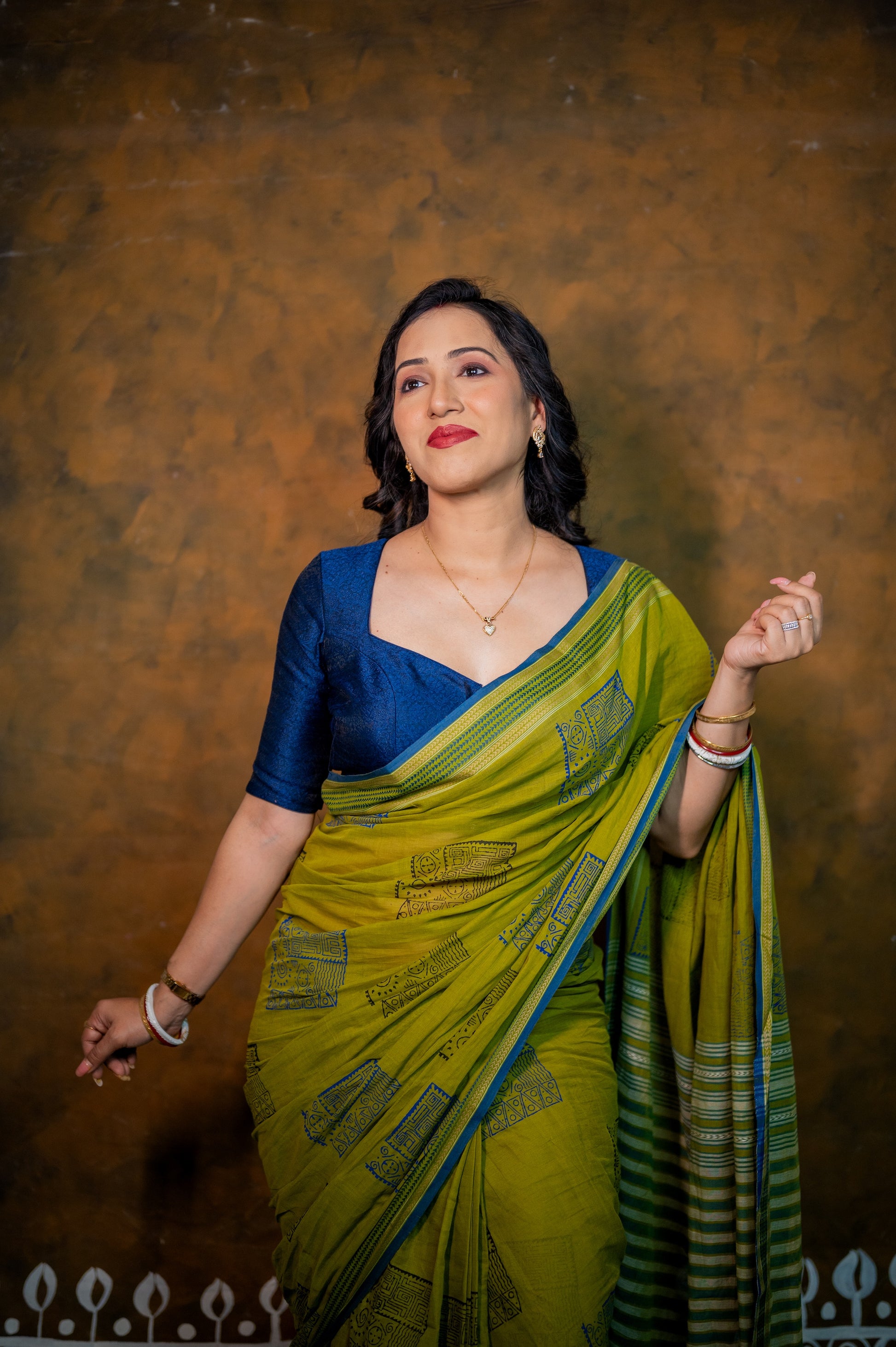 Close-up of blue jamebar blouse with deep neckline, styled with a green saree and minimal accessories.