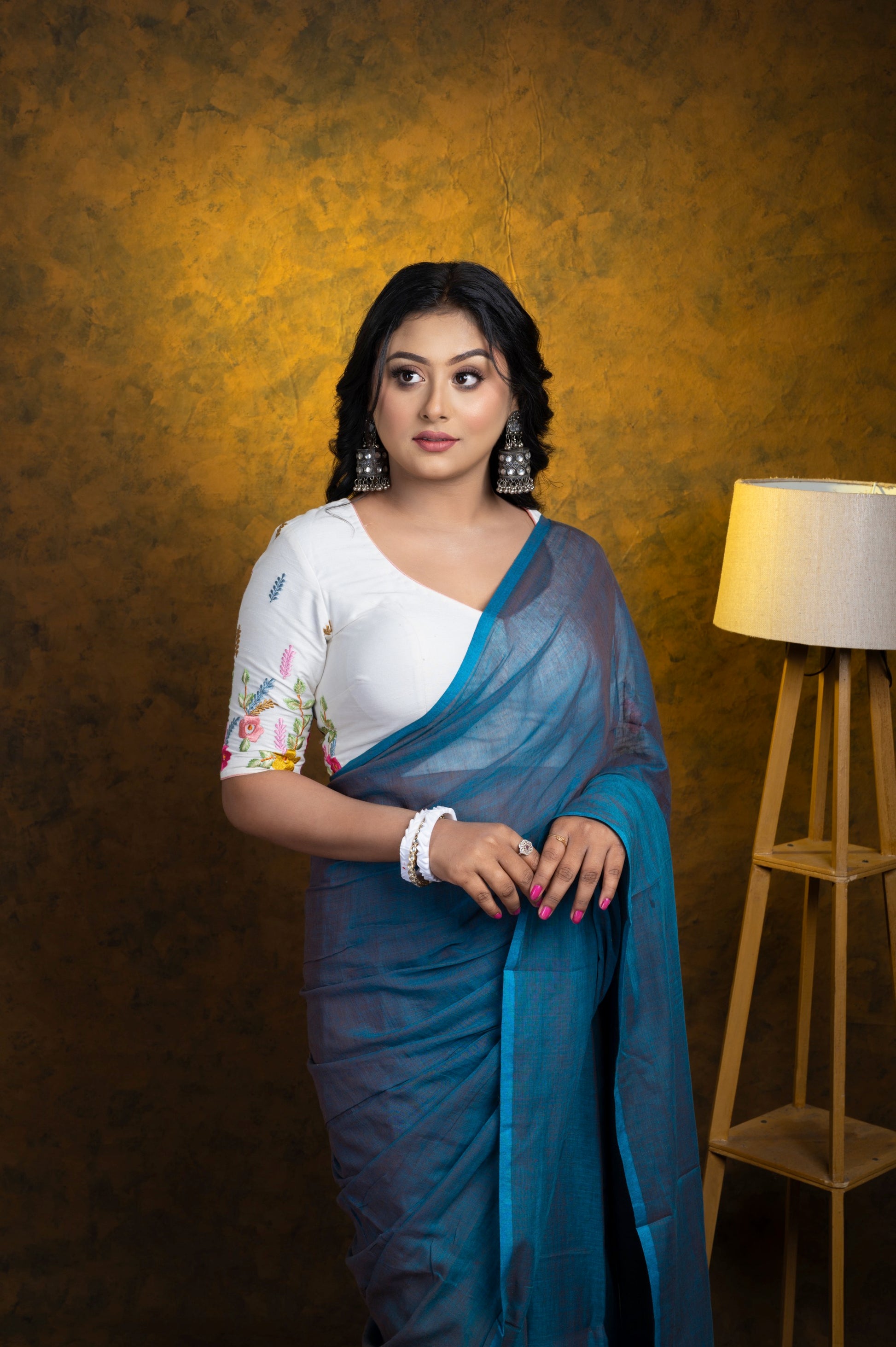 Full-length shot of a woman in a white floral-embroidered blouse and soft blue cotton saree, styled for effortless everyday elegance.