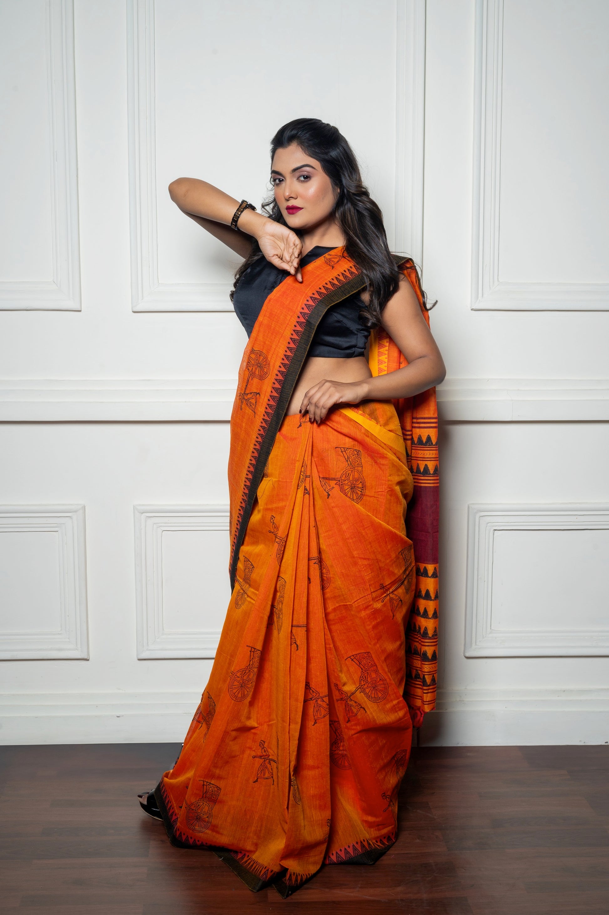 Full-length image of the model in the black blouse and vibrant saree, striking a power pose against a white panel background.