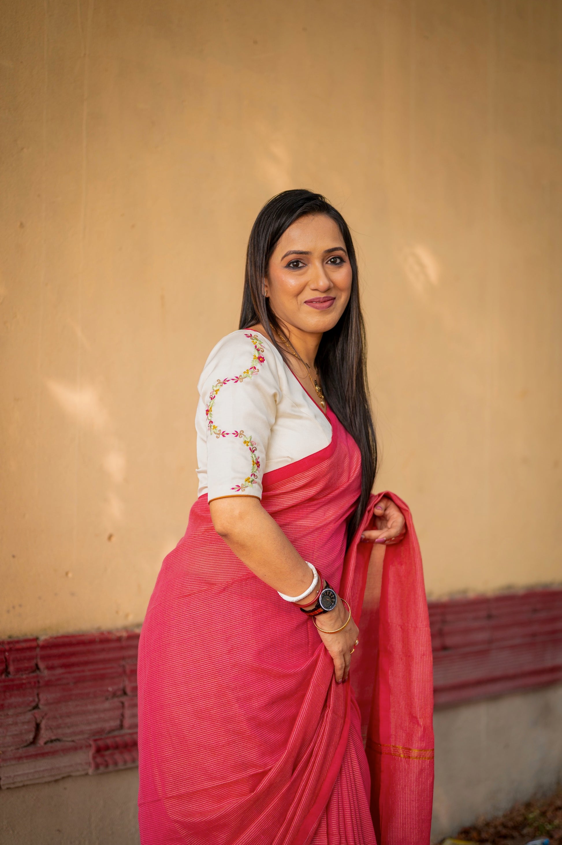 Side view of an off-white semi-silk blouse with floral embroidery and a triple teardrop designer cut, styled with a red handwoven saree.