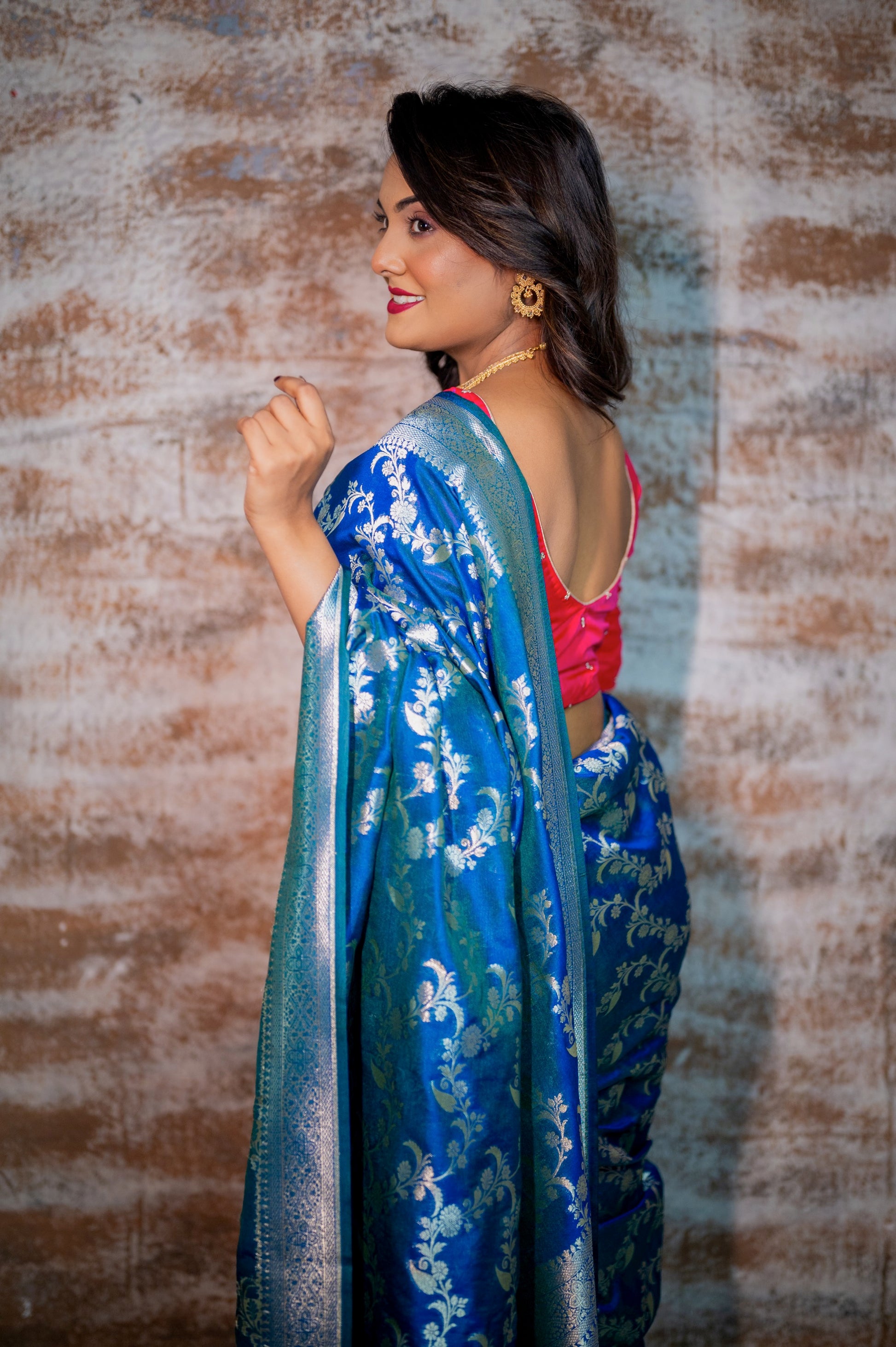 Back view of deep-cut rani pink blouse with pearl accents styled with a traditional blue saree.