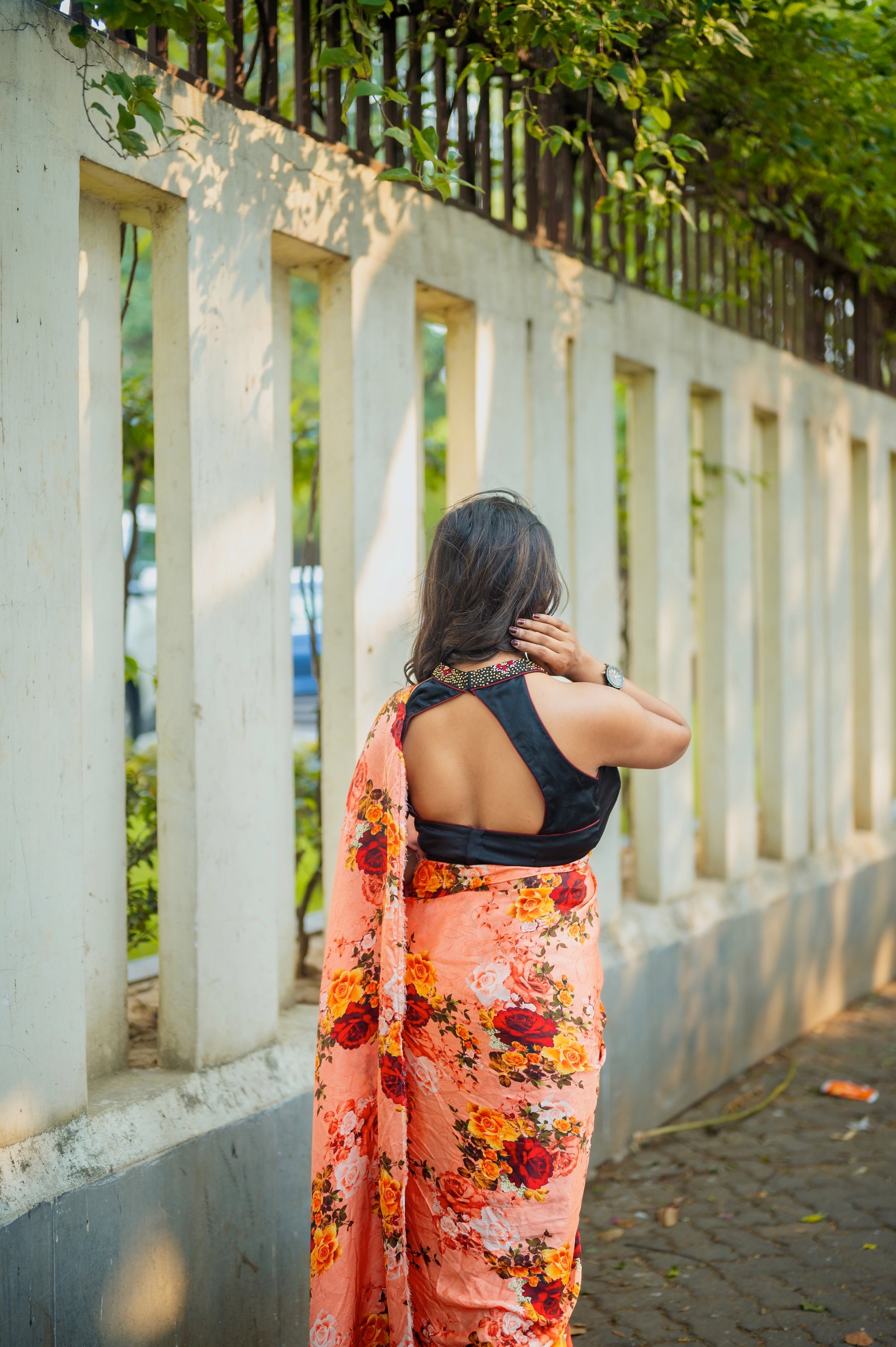 Rear pose showing the black blouse’s open-back halter cut with zardozi neckline, contrasted by a peach floral saree.