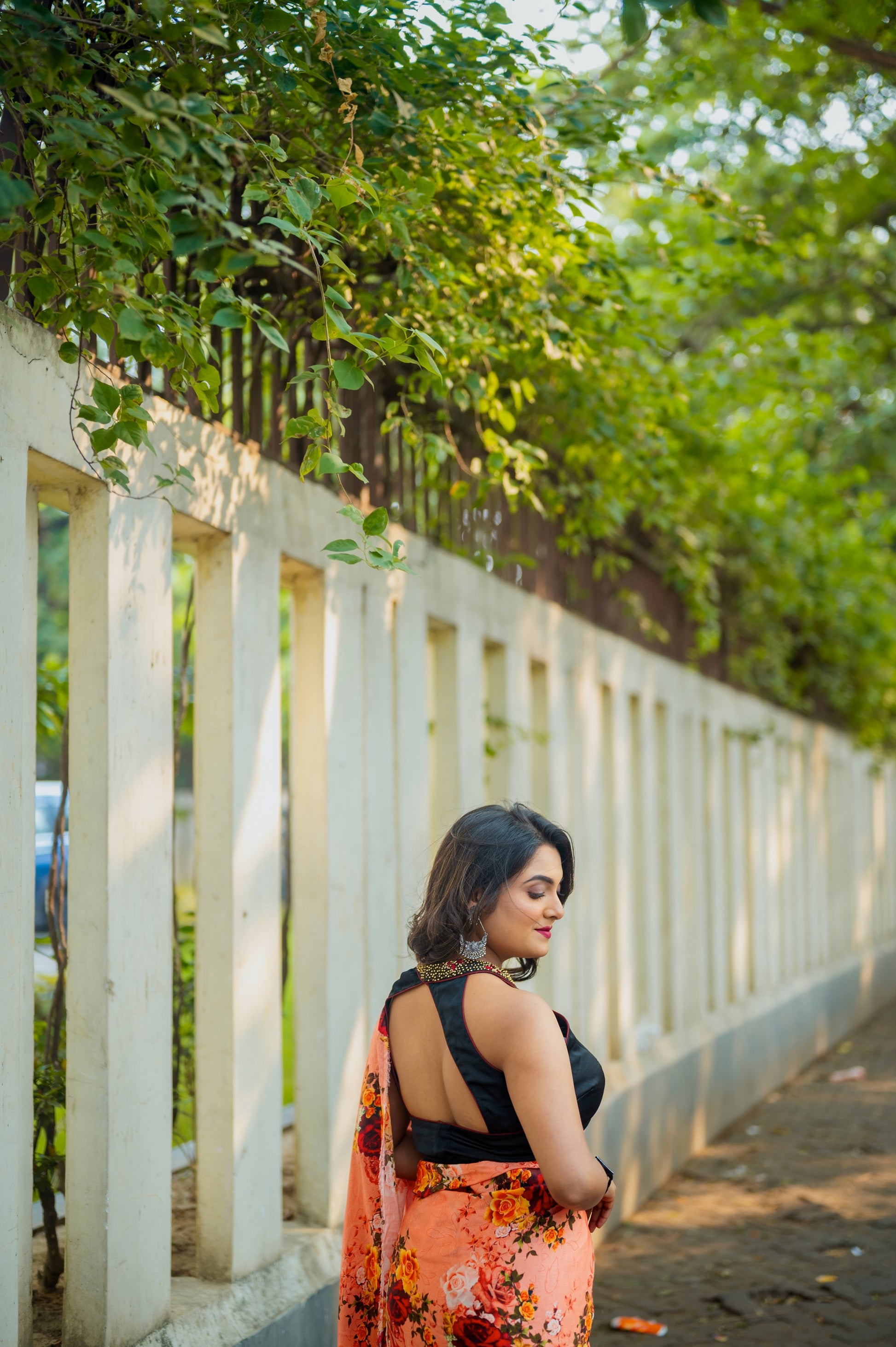Diagonal back view of the halter-style blouse with embroidered neckline, styled with a flowing floral saree outdoors.