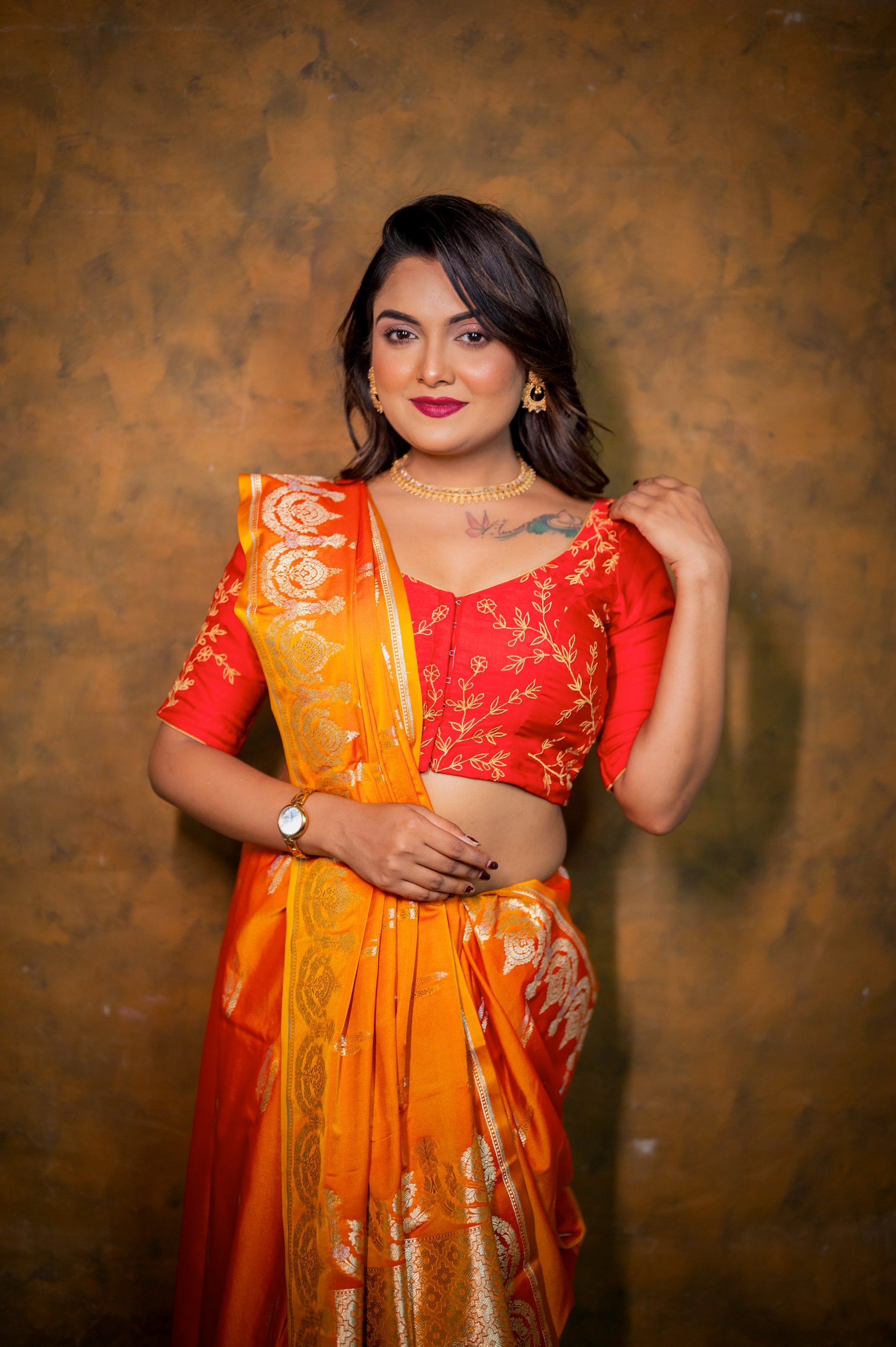 Close-up of red embroidered blouse with traditional golden jari work, styled with an orange saree and gold jewelry.