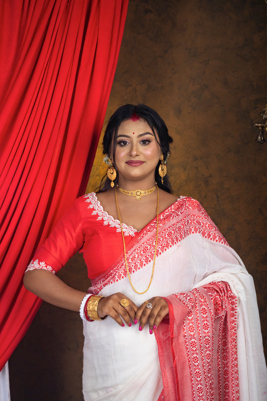 Front view of bold red semi-silk blouse with wide V neckline and white thread embroidery, paired with red-bordered saree and traditional gold jewelry