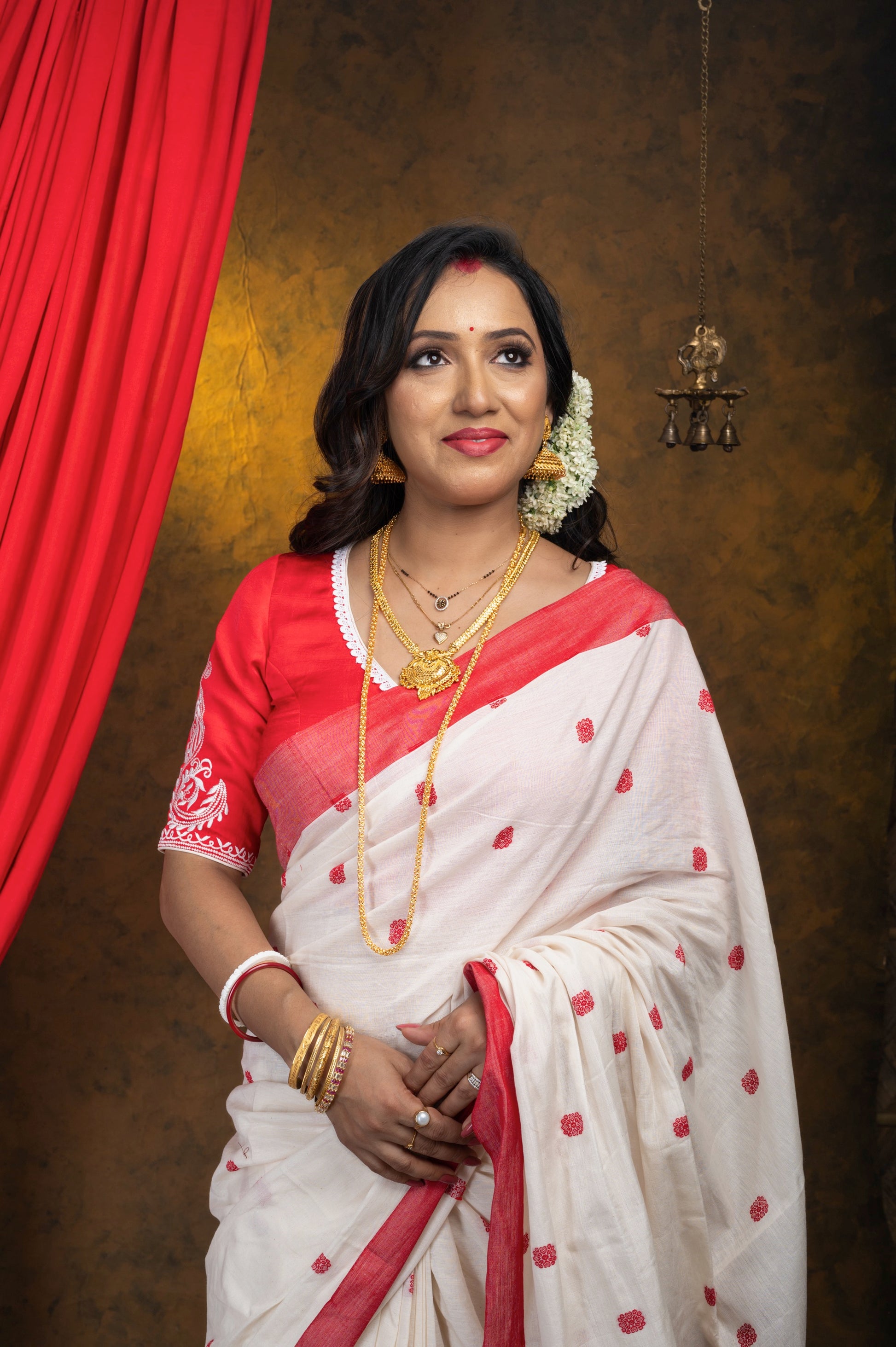 Portrait of woman in red semi-silk blouse with detailed off-white embroidery on sleeves and neckline, paired with red and white saree, accessorized with gold jewelry and gajra