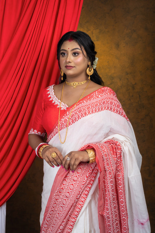 Side-angled front view of red blouse with elegant off-white embroidery and wide neckline, styled with traditional white saree and layered gold jewelry for festive occasions