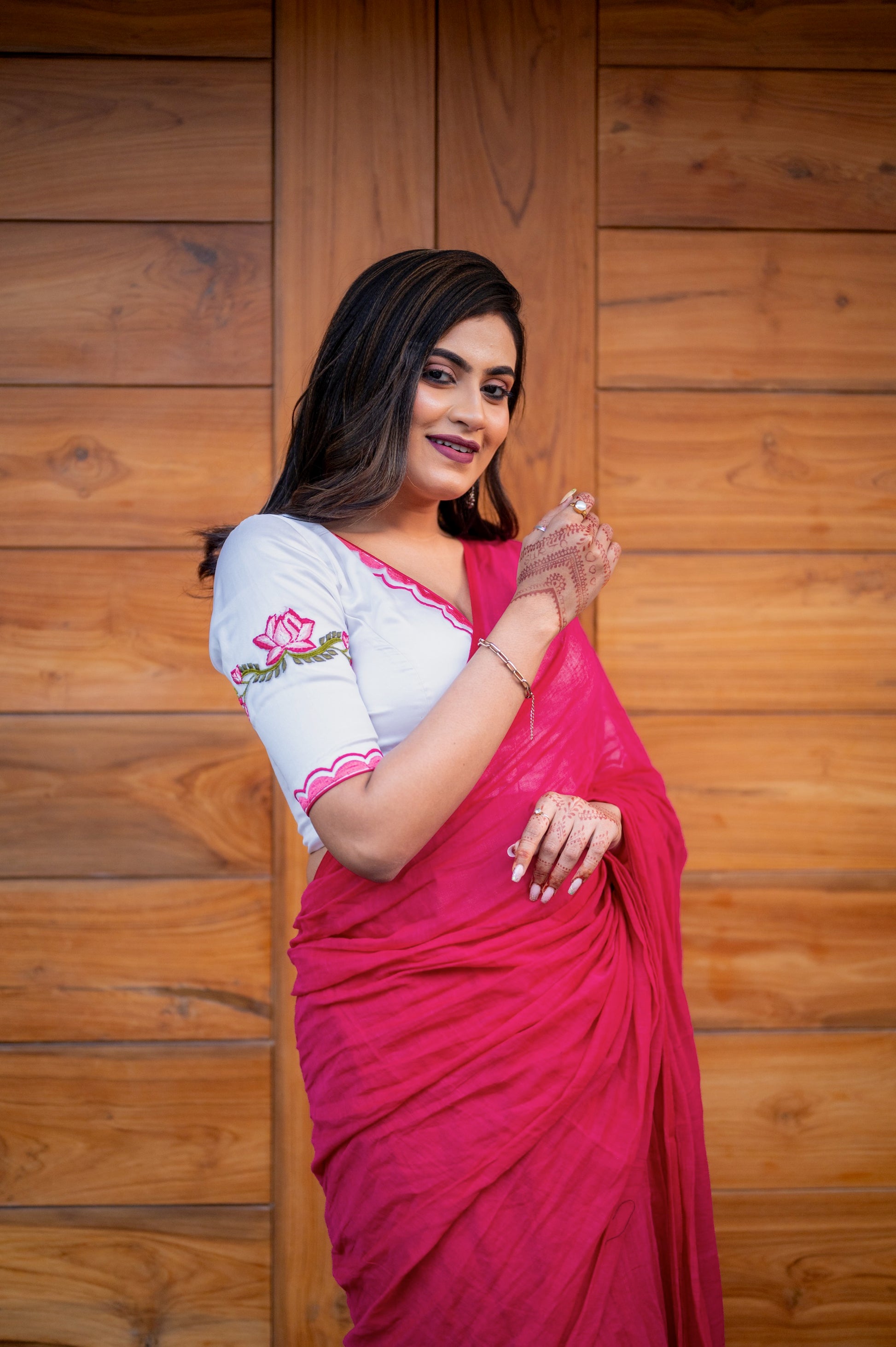 A woman in a white organza blouse with pink lotus embroidery on the sleeve and a wide V neckline, paired with a bright pink chiffon saree.
