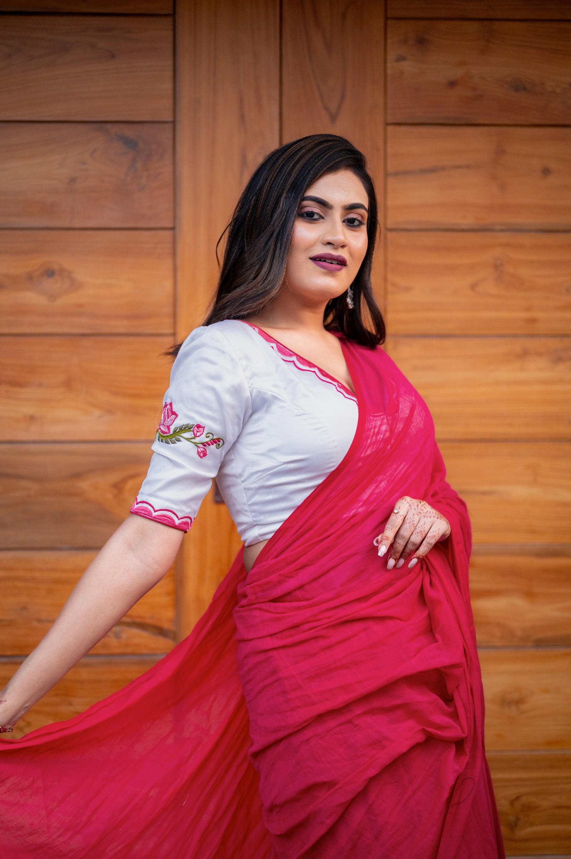 Side pose of a woman in a soft white organza blouse with lotus embroidery on the sleeve and neckline, styled with a vibrant pink saree.