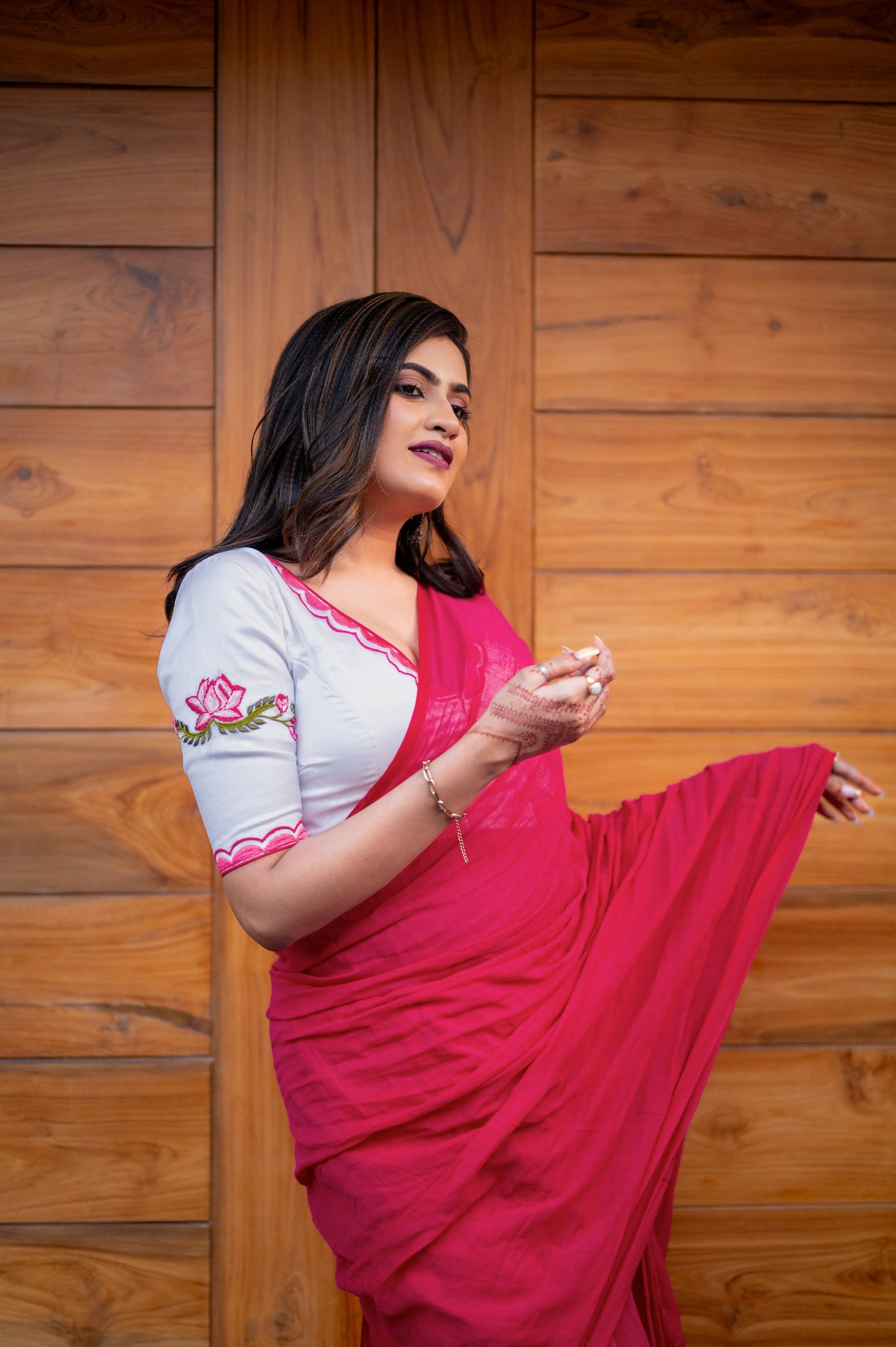 A woman poses gracefully in a white organza blouse with lotus embroidery and pink scallop trim, draped in a chiffon saree.