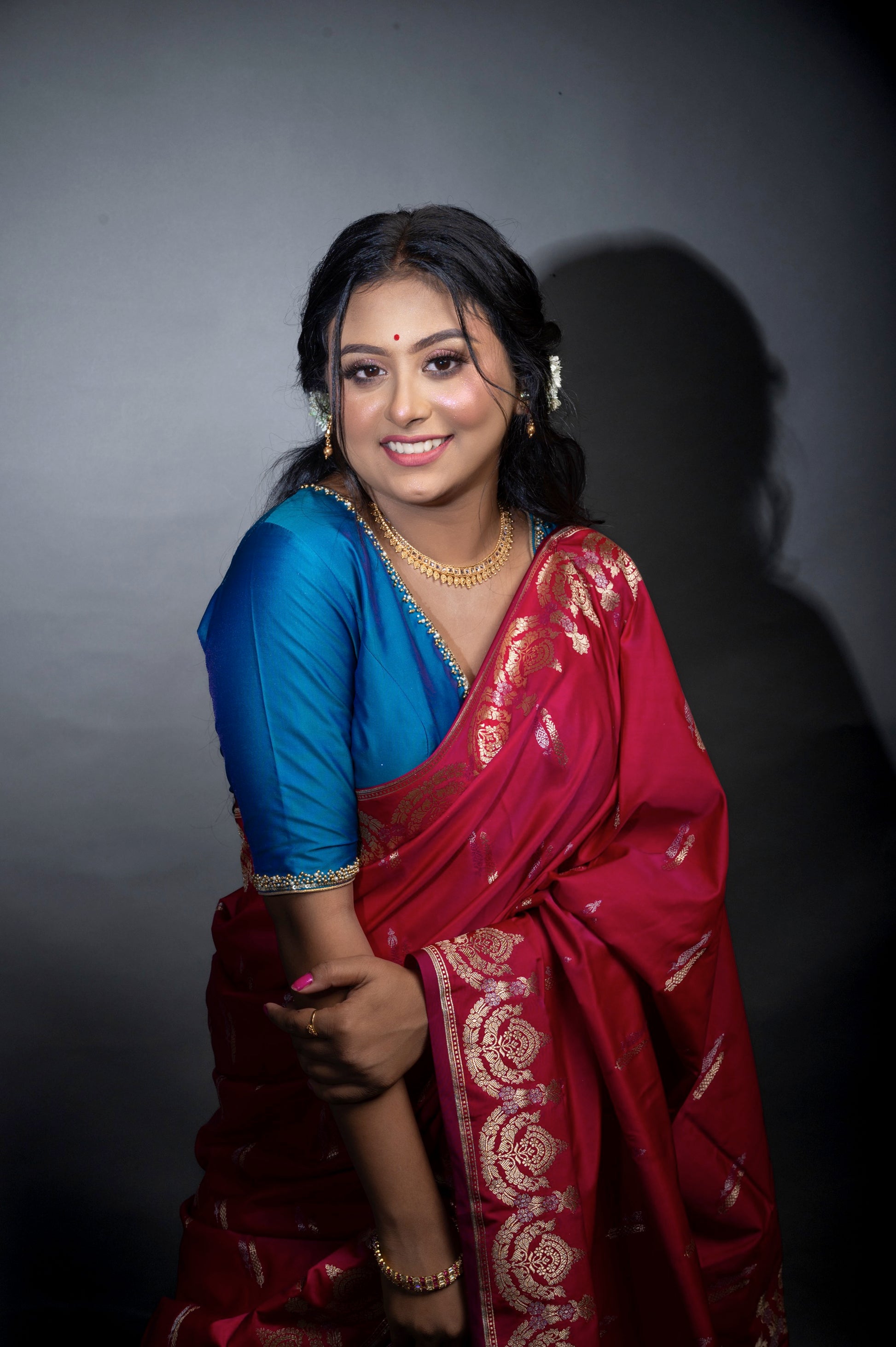 Close-up side view of a woman in a deep teal blouse with shimmering sleeve borders and plunging neckline, paired with a contrasting red saree for an elegant festive look.