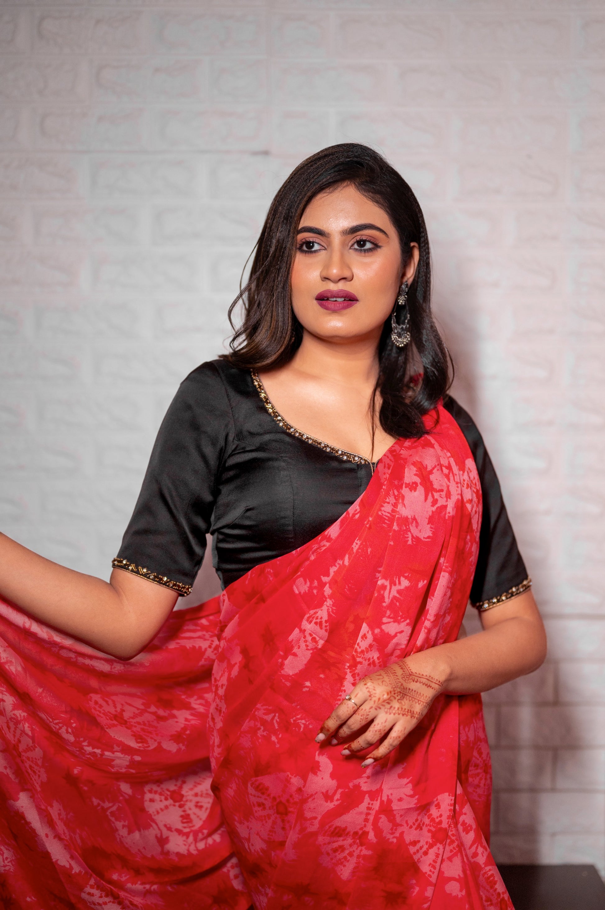 Front view of a designer black blouse featuring zardozi and jarkan work, styled with a bright red printed chiffon saree.