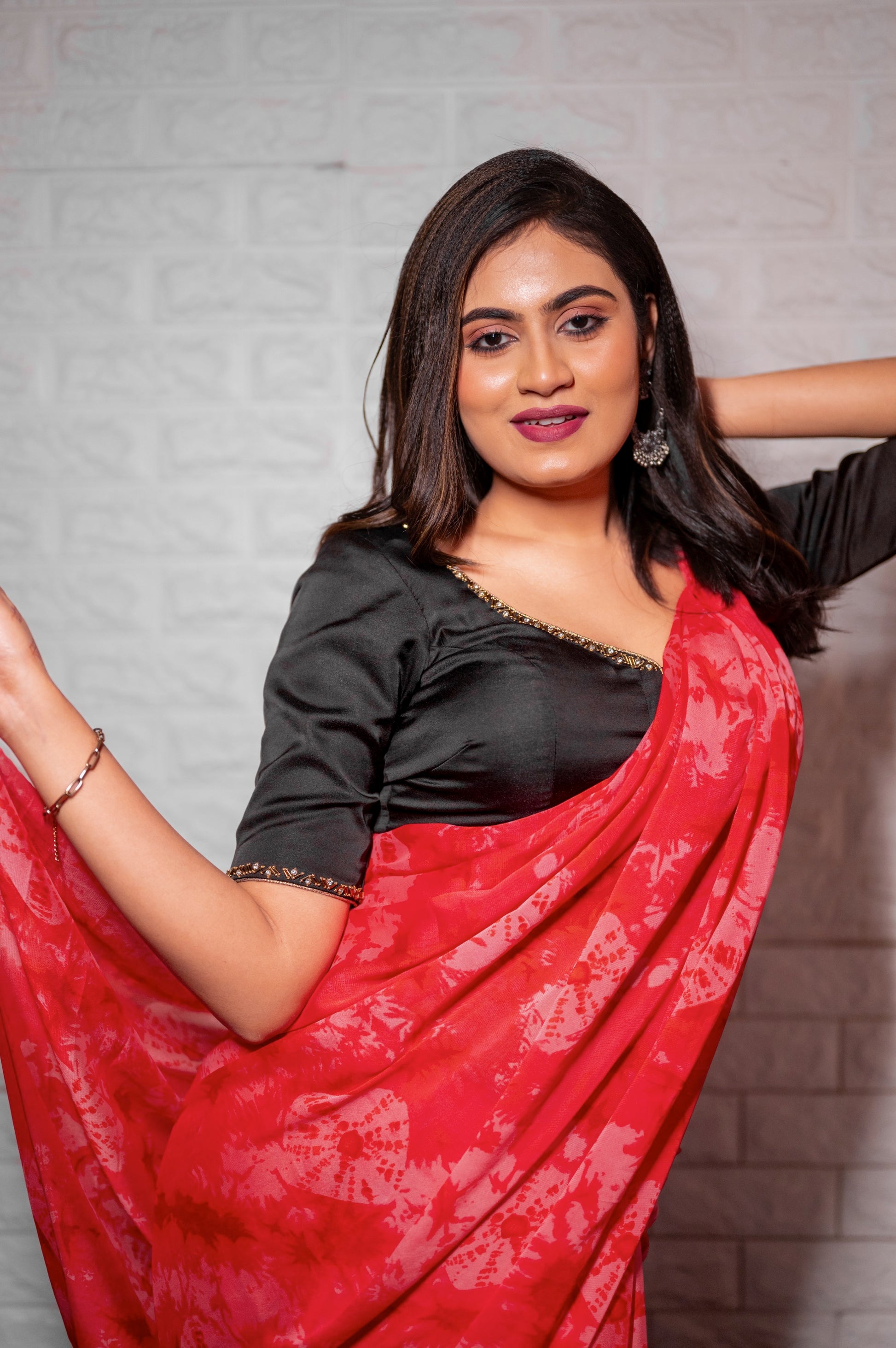 Woman wearing a black semi-silk blouse with embellished neckline and sleeves, styled with a red saree and oxidized earrings.