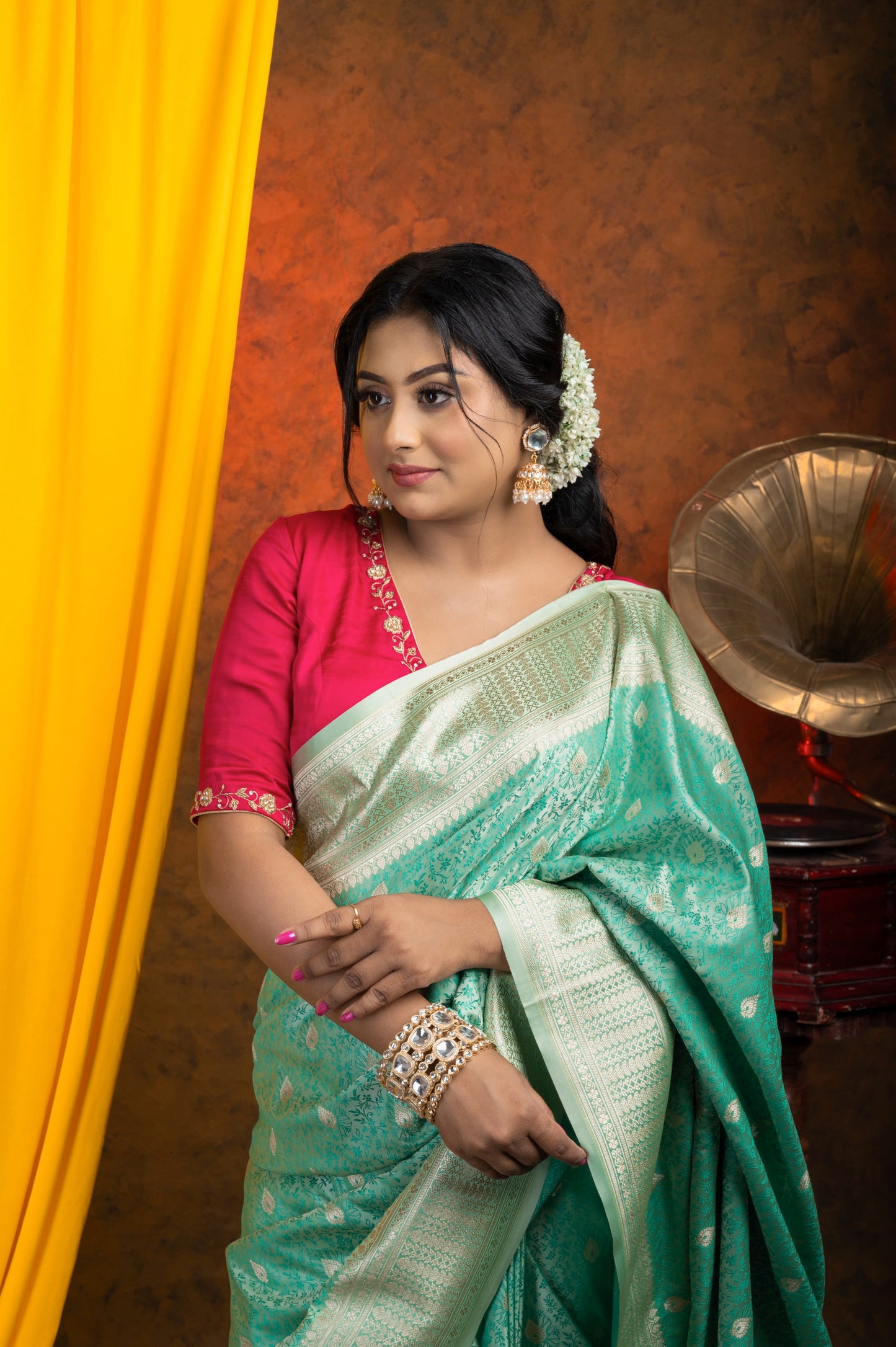 Front view of rani pink semi-silk blouse with golden zardozi floral embroidery on neckline and sleeves, paired with a mint green silk saree and accessorized with gajra, earrings, and statement bangles