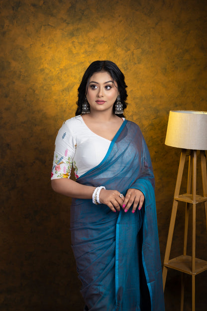 Full-length shot of a woman in a white floral-embroidered blouse and soft blue cotton saree, styled for effortless everyday elegance.