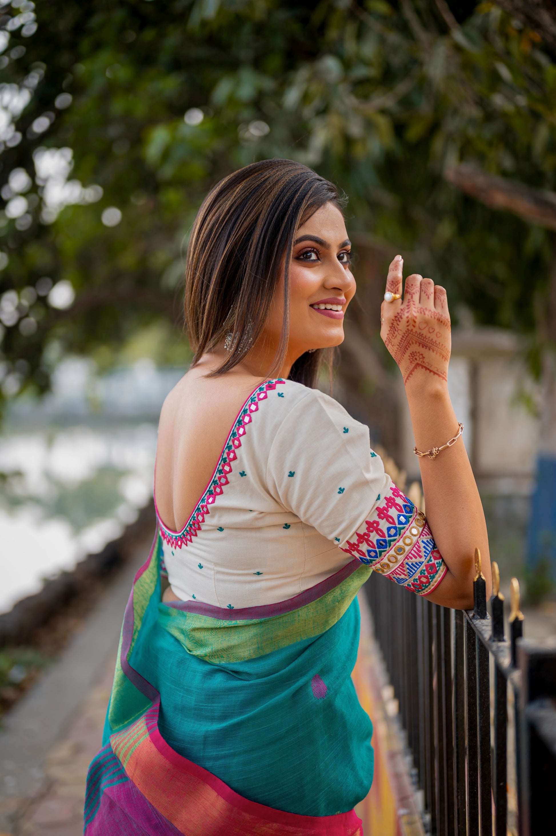 Side view of a Woman in a white cotton-linen blouse with colorful mirror work and embroidery, showing the deep V-cut back while posing outdoors.