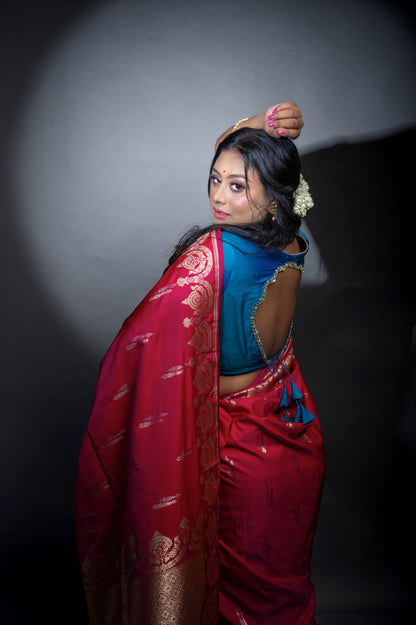  Close-up side view of a woman in a deep teal blouse with shimmering sleeve borders and plunging neckline, paired with a contrasting red saree for an elegant festive look.